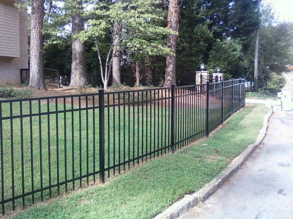 Black flat-top aluminum fence along a Brookhaven, GA street with stone entrance columns, installed by FenceWorks of Georgia