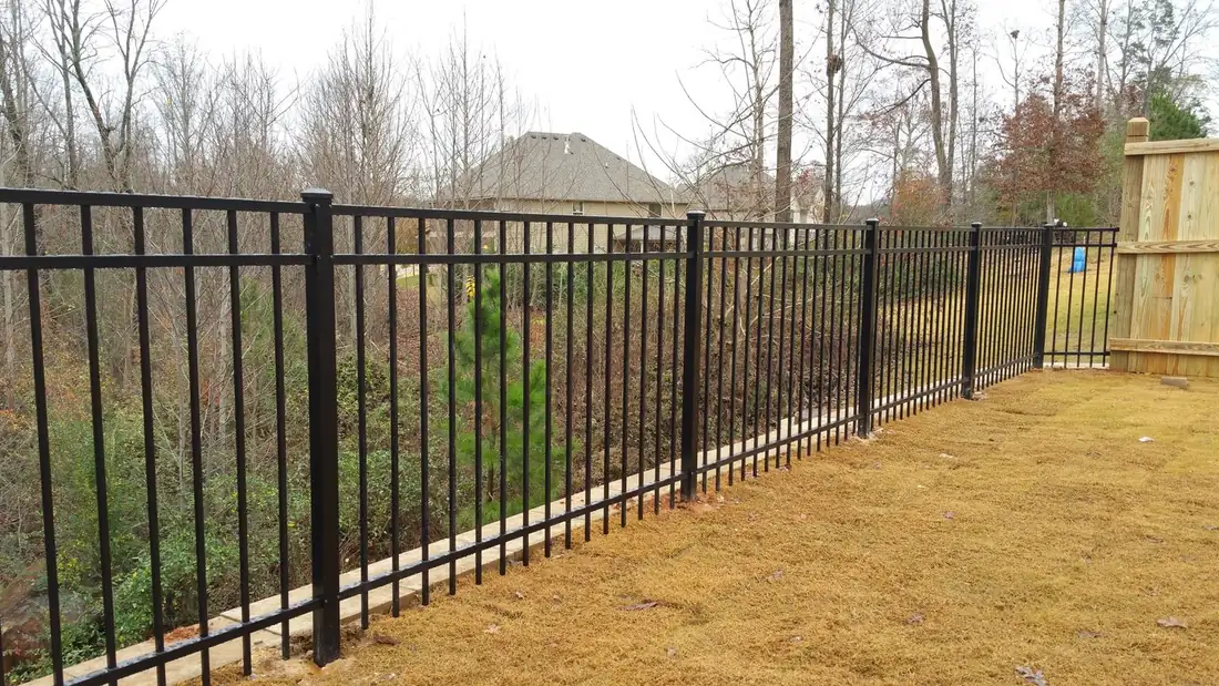 Black aluminum flat-top three-rail fence running along a wooded back property line, installed by FenceWorks of Georgia