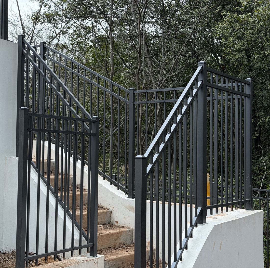 Black aluminum stair railing with square balusters running along a poured-concrete stairway in Sandy Springs, installed by FenceWorks of Georgia
