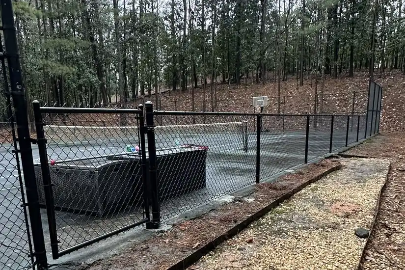 Black chain-link fencing enclosing a private tennis and basketball court