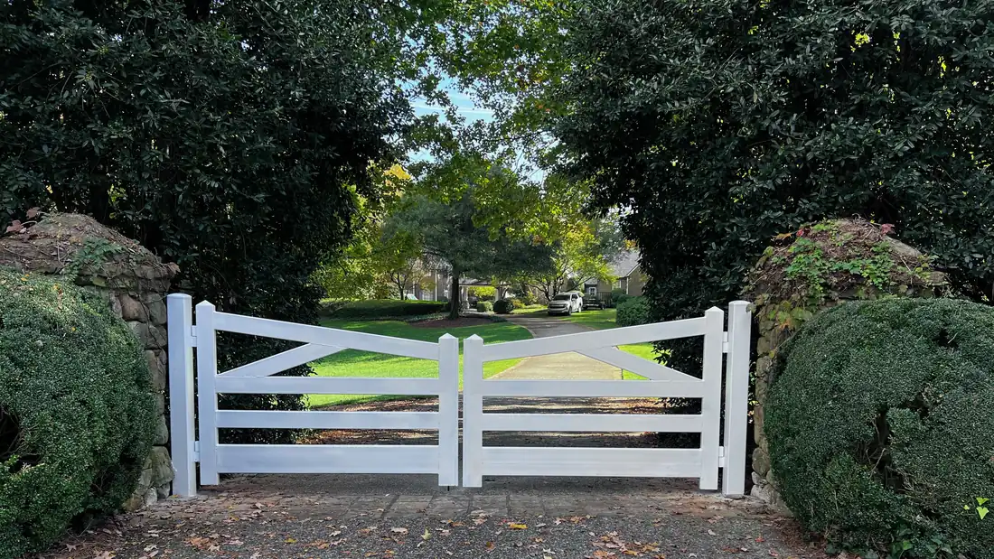 Custom white aluminum double driveway gate set between stone pillars and clipped hedges at a residential drive, built by FenceWorks of Georgia