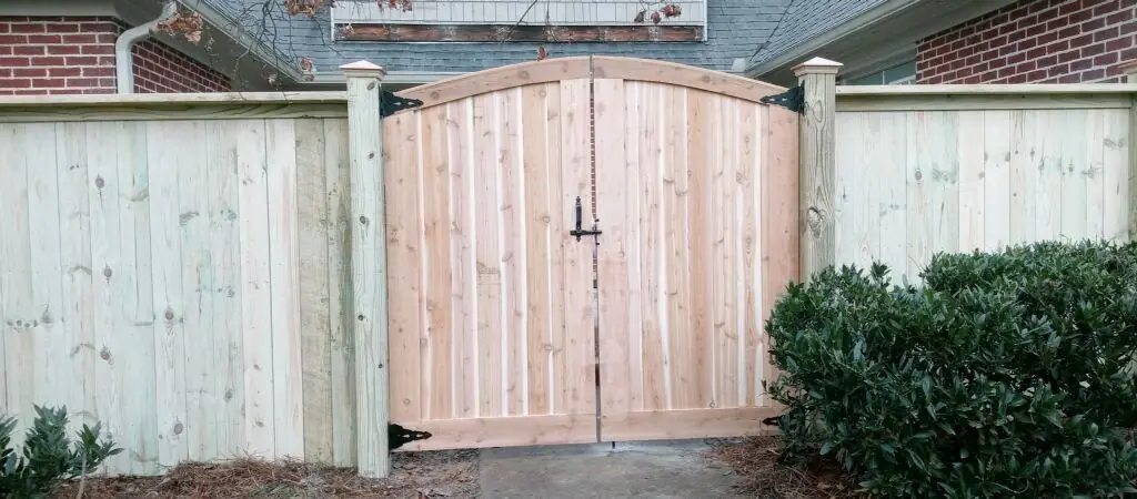 Arched cedar double gate set into a wood privacy fence beside a brick home, built by FenceWorks of Georgia