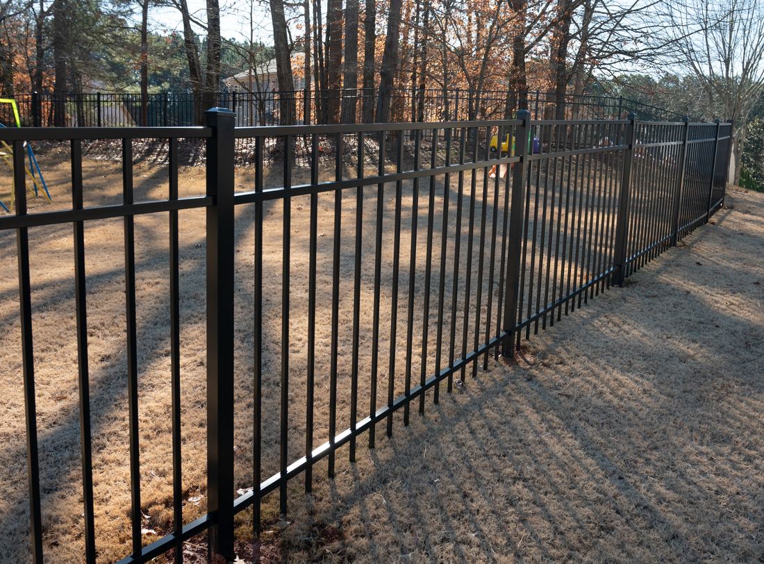 Black flat-top aluminum fence enclosing a wooded residential back yard, installed by FenceWorks of Georgia