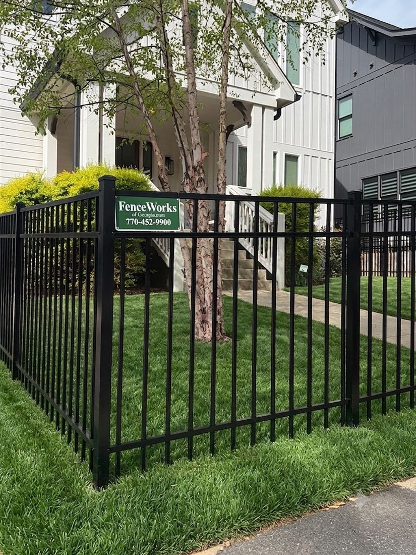 Black flat-top aluminum front-yard fence with a FenceWorks of Georgia job sign