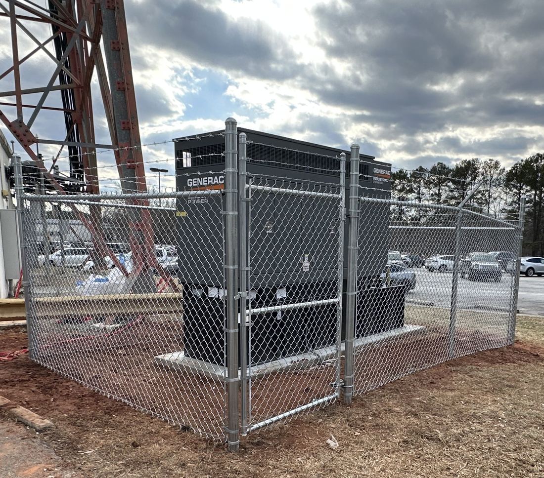 Galvanized chain-link security enclosure with barbed wire around a standby generator, installed by FenceWorks of Georgia