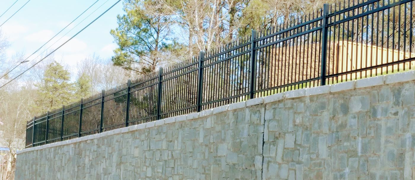 Black spear-top ornamental steel fence atop a stacked-stone retaining wall