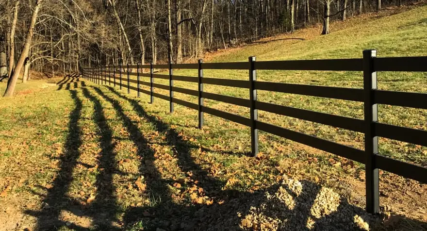 Black four-rail Buckley steel-board horse fence running down a sunlit pasture toward the treeline, installed by FenceWorks of Georgia