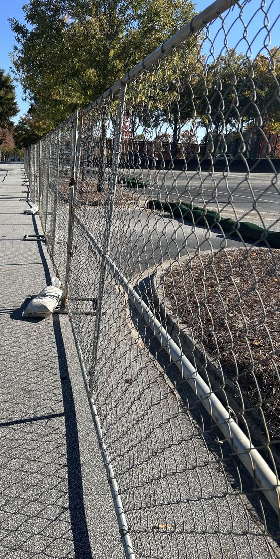 Temporary chain-link panel fencing installed along a parking lot for a job site