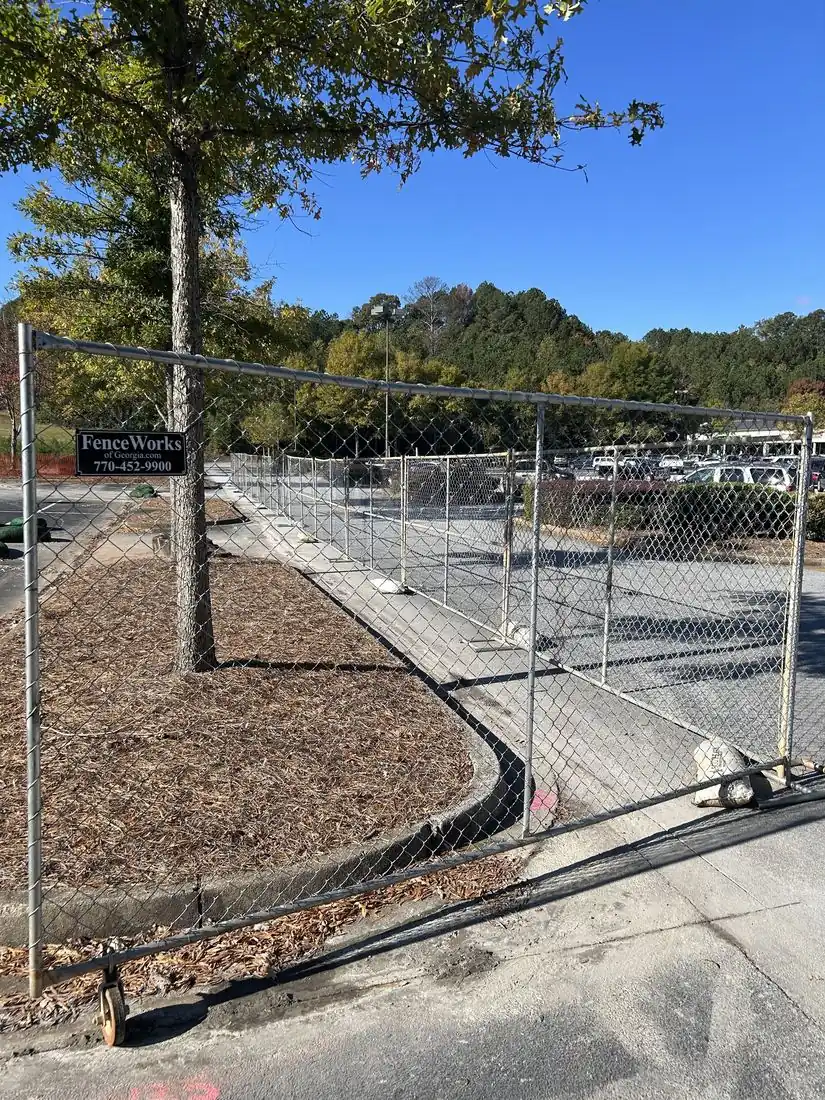 Temporary chain-link panel fence and rolling gate securing a commercial parking lot job site