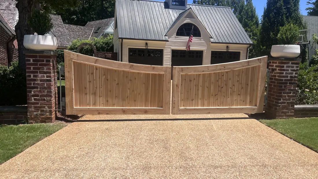 Arched cedar double driveway gate between brick columns at a residential entrance, built by FenceWorks of Georgia