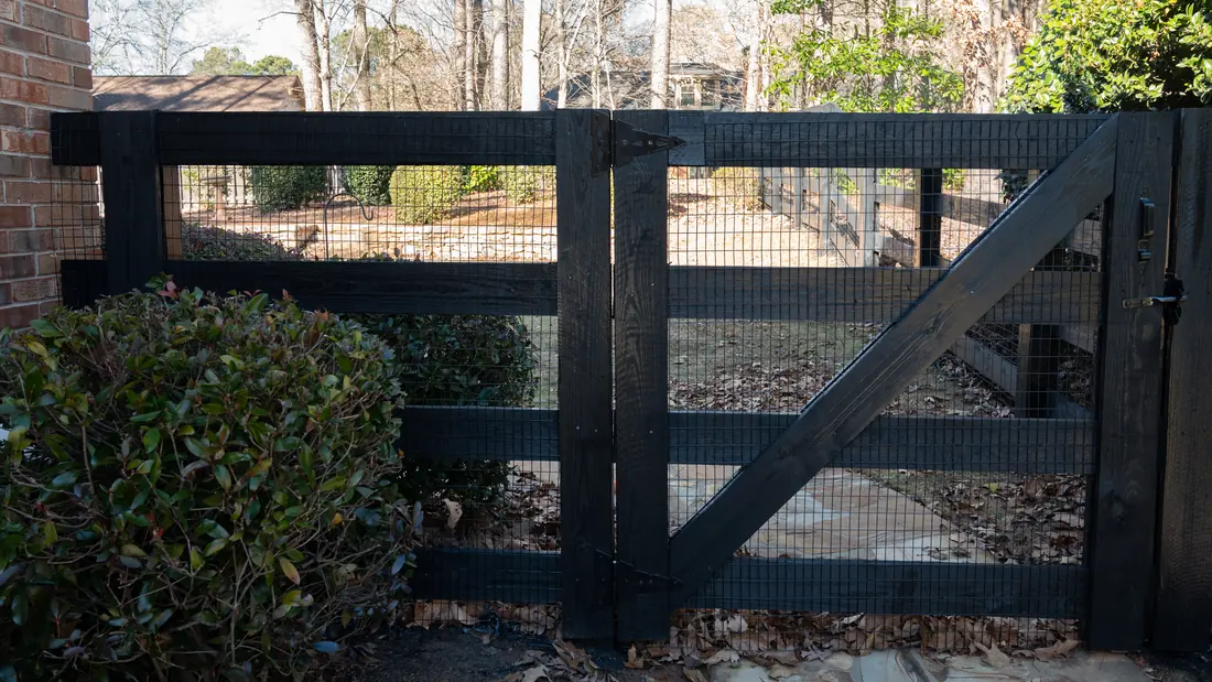 Black-stained wood four-rail ranch fence and matching double gate backed with welded wire, built by FenceWorks of Georgia