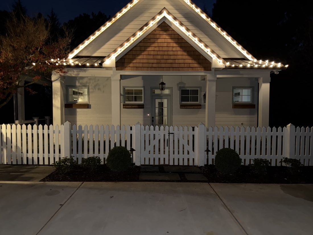 White wood picket fence with rooftop pickets and 6x6 rooftop posts in front of a lit cottage, built by FenceWorks of Georgia