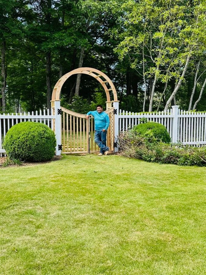 Arched wooden arbor with a walk gate set into a white picket fence