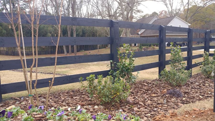 Black four-rail wooden ranch fence with fresh landscaping on a larger lot