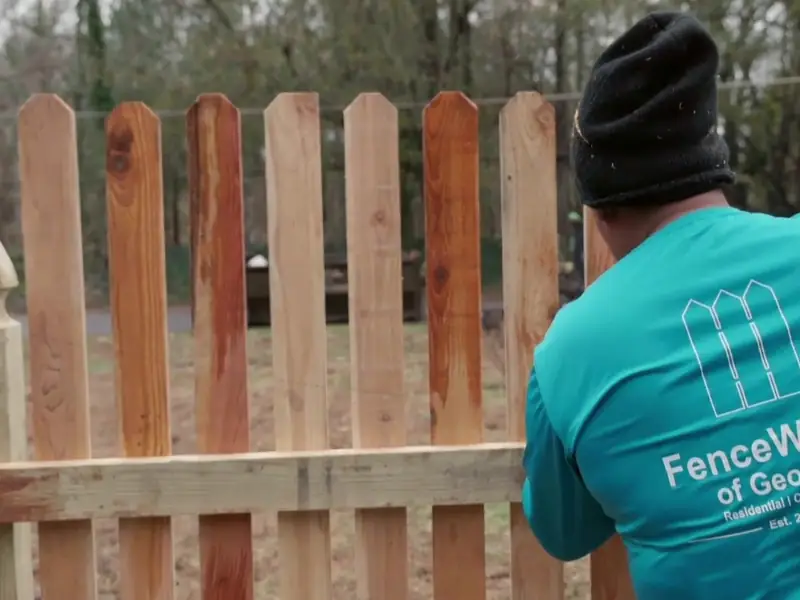 FenceWorks of Georgia crew member in a FenceWorks shirt hanging cedar pickets between French gothic posts