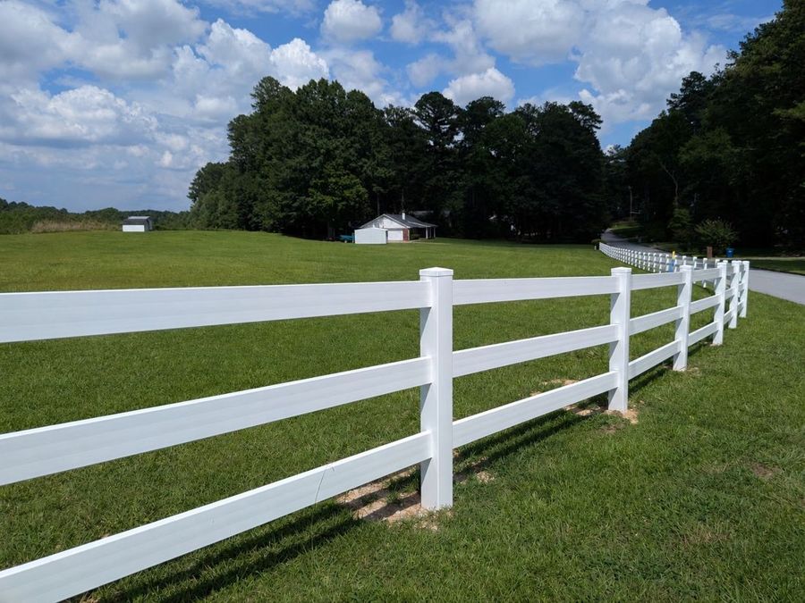 White vinyl three-rail ranch fence running along a green pasture